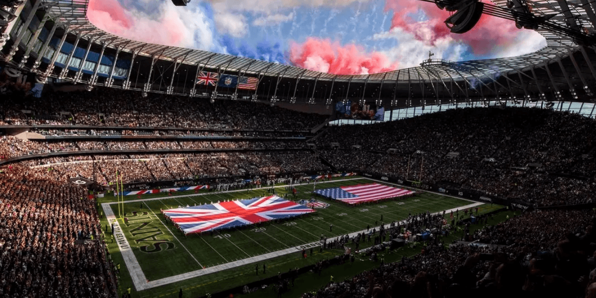 Packed stadium with British and American flags on the field under a colorful sky