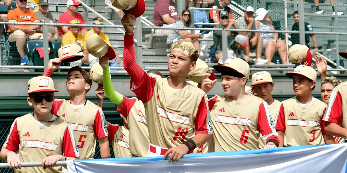 Young baseball players in uniforms waving hats and holding a banner at a game