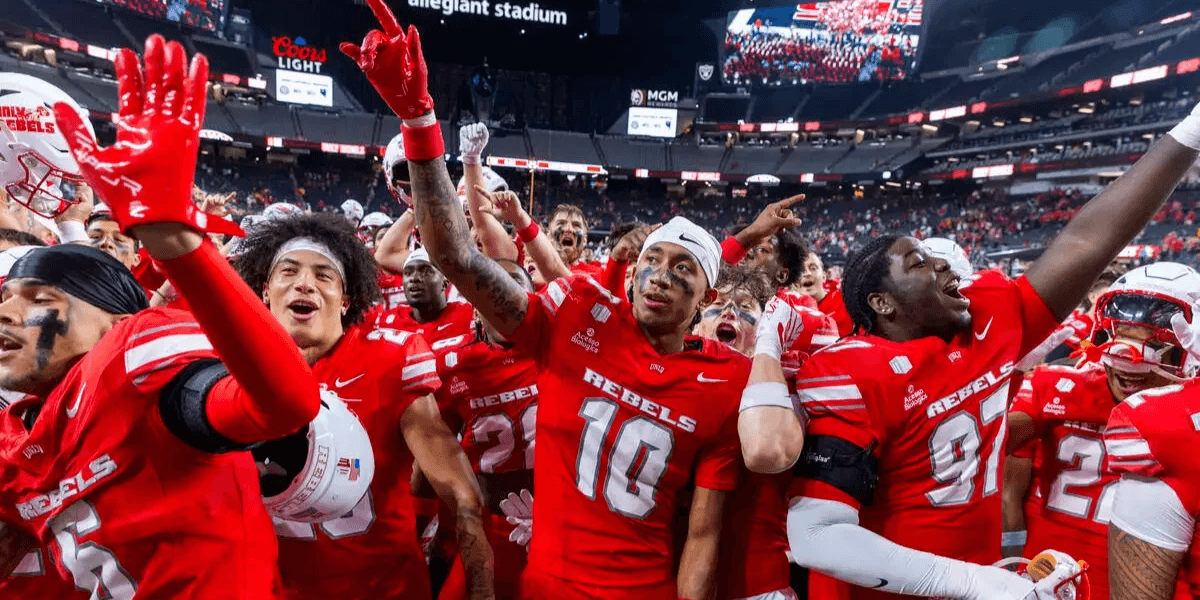 A football team celebrating on the field, wearing red uniforms, amidst cheering fans