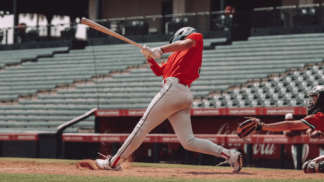 Baseball player swings at a pitch during an MLB game as the catcher reaches for the ball behind home plate.