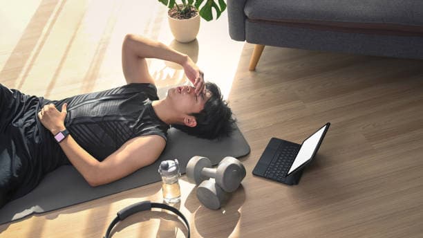 Tired young man lying on mat after exercises in living room.