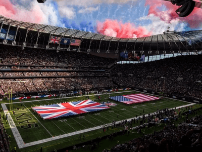 Packed stadium with British and American flags on the field under a colorful sky
