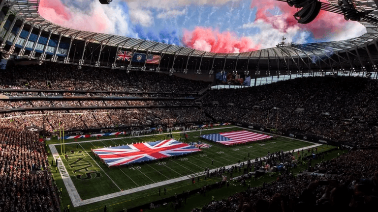 Packed stadium with British and American flags on the field under a colorful sky