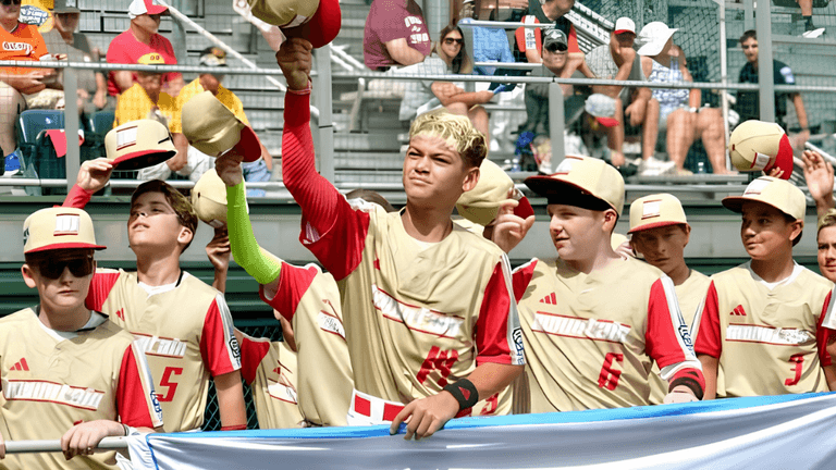 Young baseball players in uniforms waving hats and holding a banner at a game