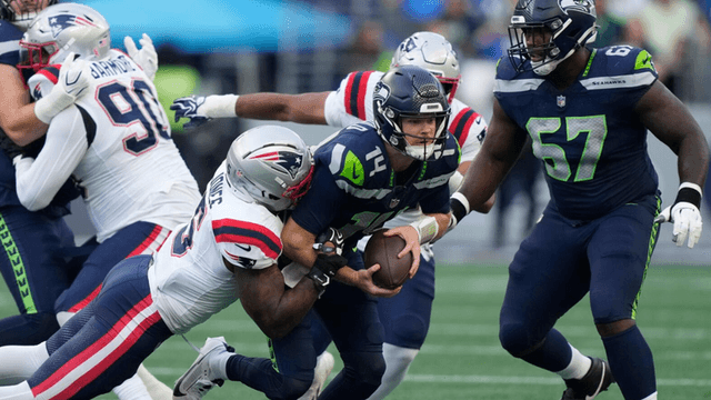 Seahawks quarterback being tackled by Patriots players during an NFL game action shot