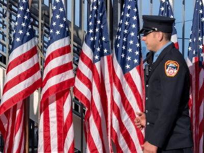 A uniformed officer walks past rows of American flags in a public space