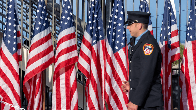 A uniformed officer walks past rows of American flags in a public space
