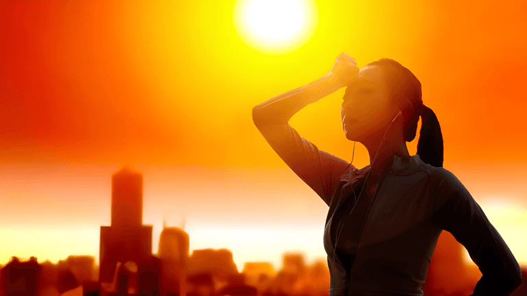 Silhouetted woman with earbuds stands against a vibrant sunset over a city skyline