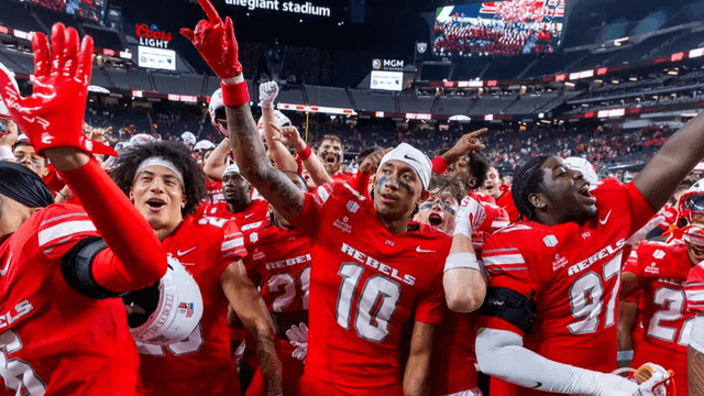 A football team celebrating on the field, wearing red uniforms, amidst cheering fans