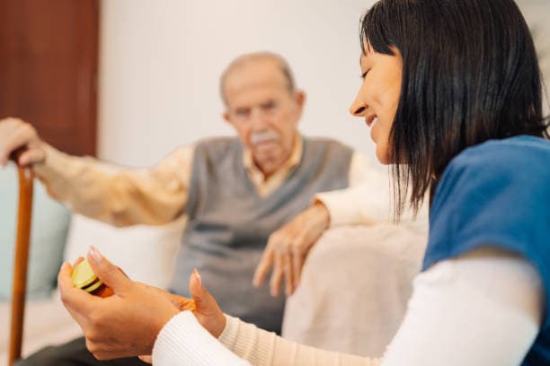 Caregiver reading instructions of pills to an elder man during a home visit