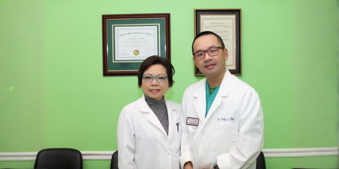 Two podiatrists in white coats standing in clinic office with framed certificates on green wall.