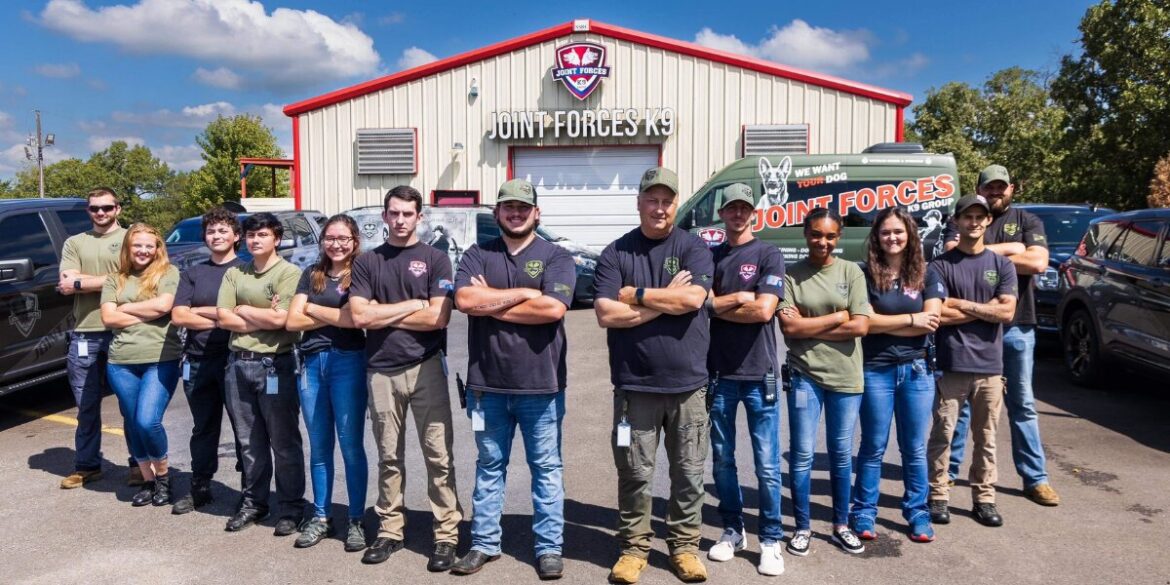 Joint Forces K9 Group team standing outside its training facility with branded vehicles behind them.