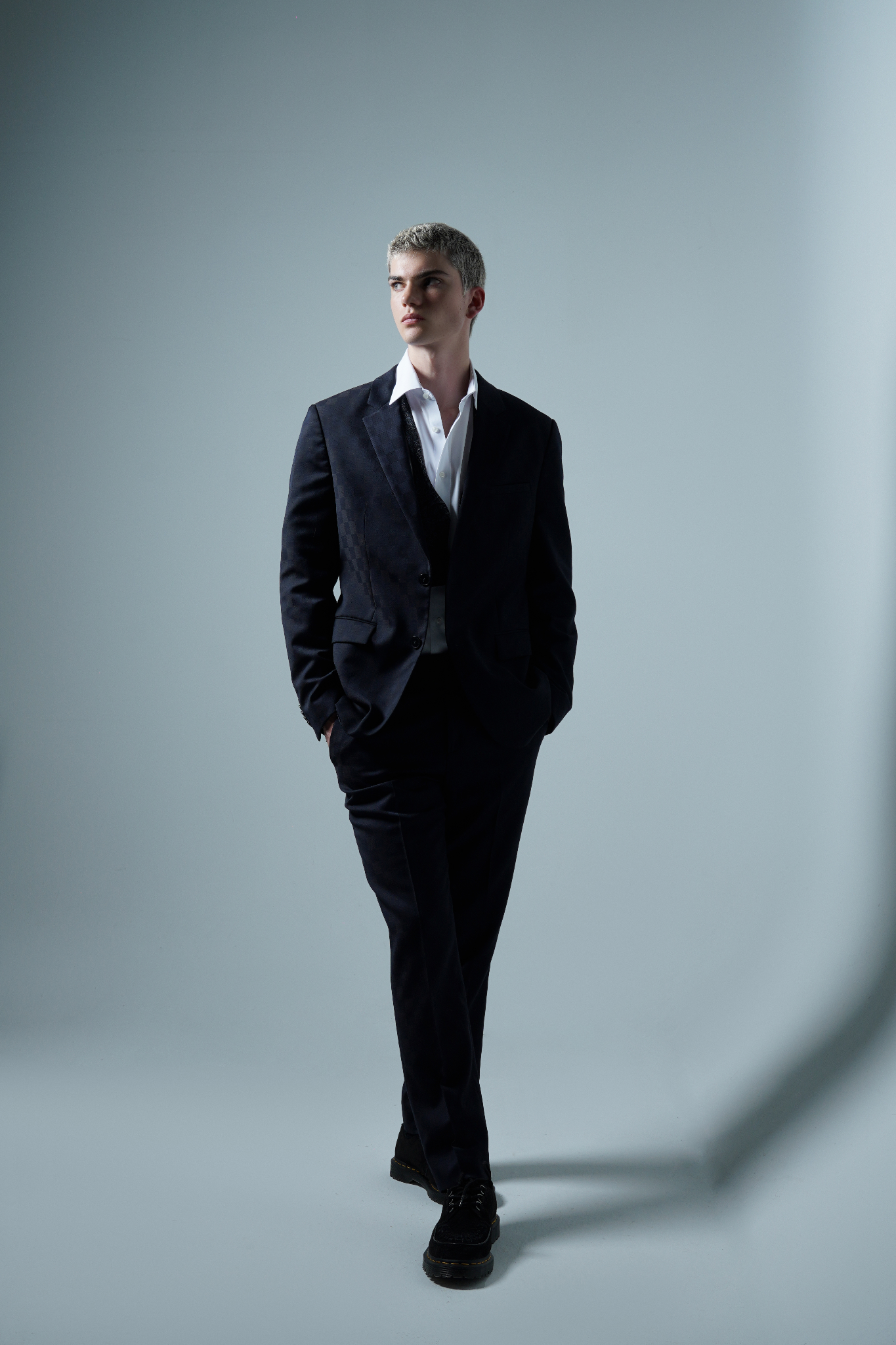 Emory Carroll walking in a tailored dark suit during a studio fashion photoshoot.