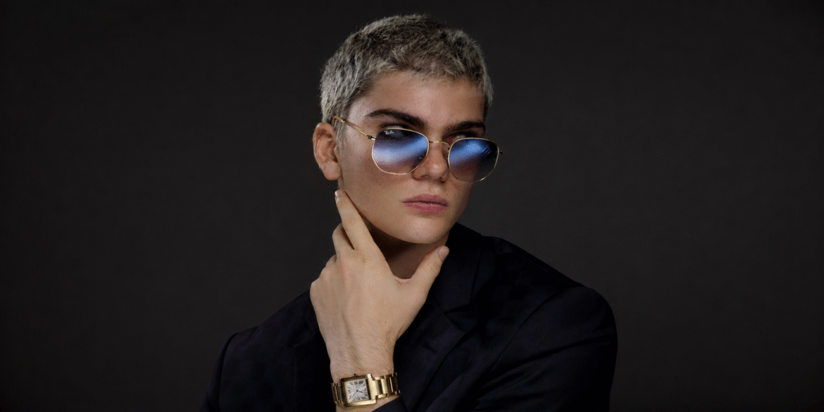 Emory Carroll wearing sunglasses, a dark suit, and a gold watch during a fashion portrait.